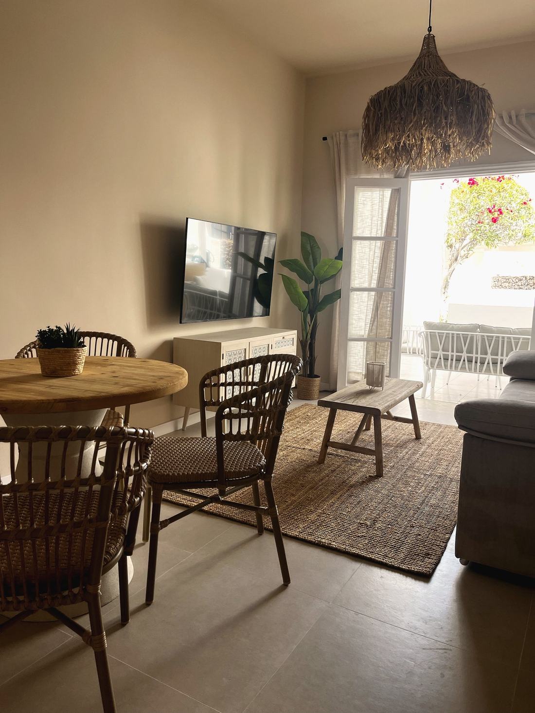 Salón comedor con mesa redonda de madera, sillas de ratán y puerta al jardín