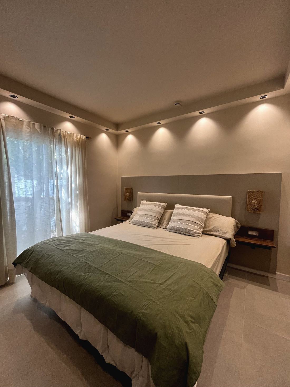 Dormitorio con cabecero tapizado, aplique de ratán y luces empotradas
