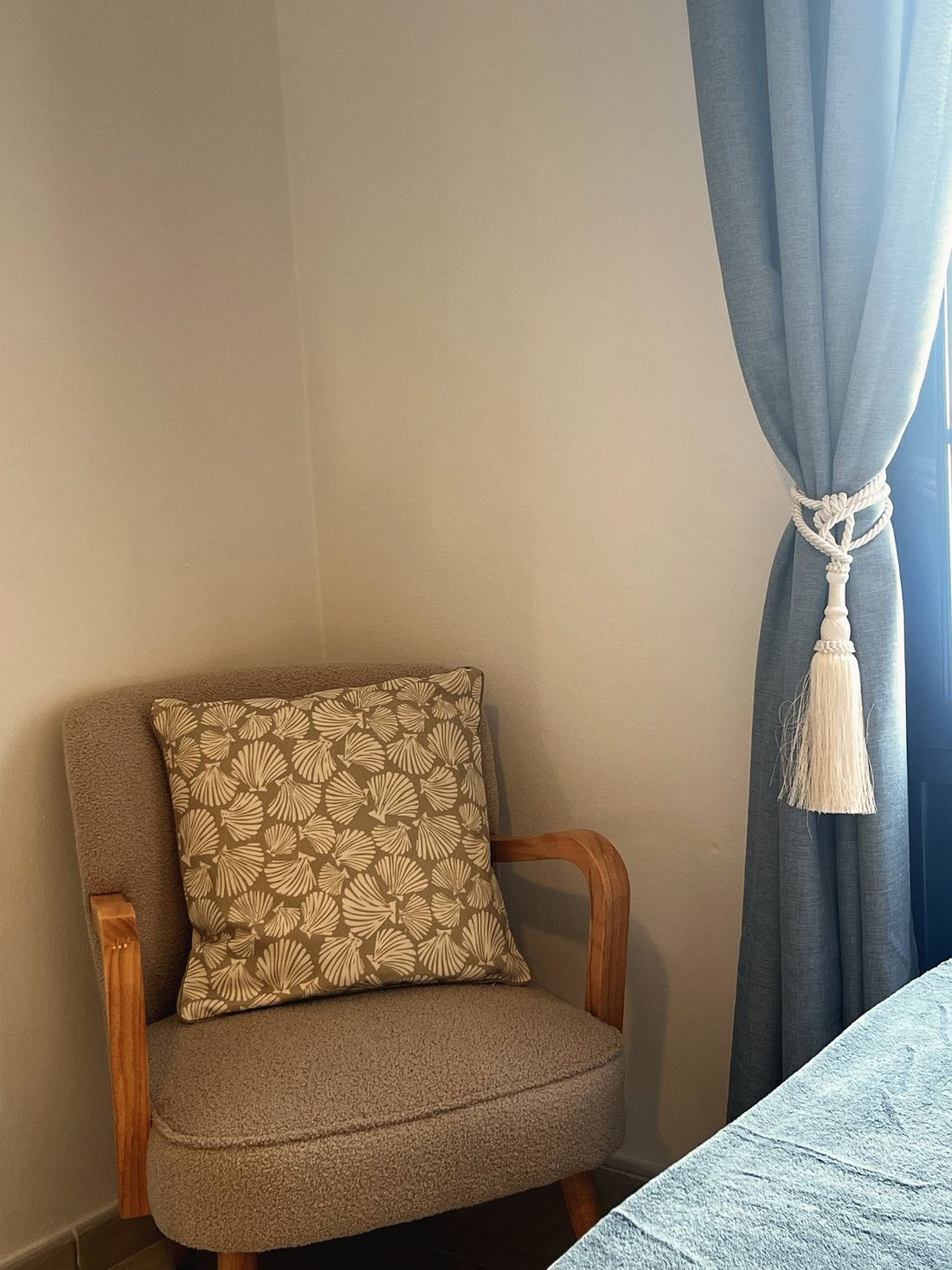 Sillón tapizado con cojín de estampado de conchas junto a la cortina azul