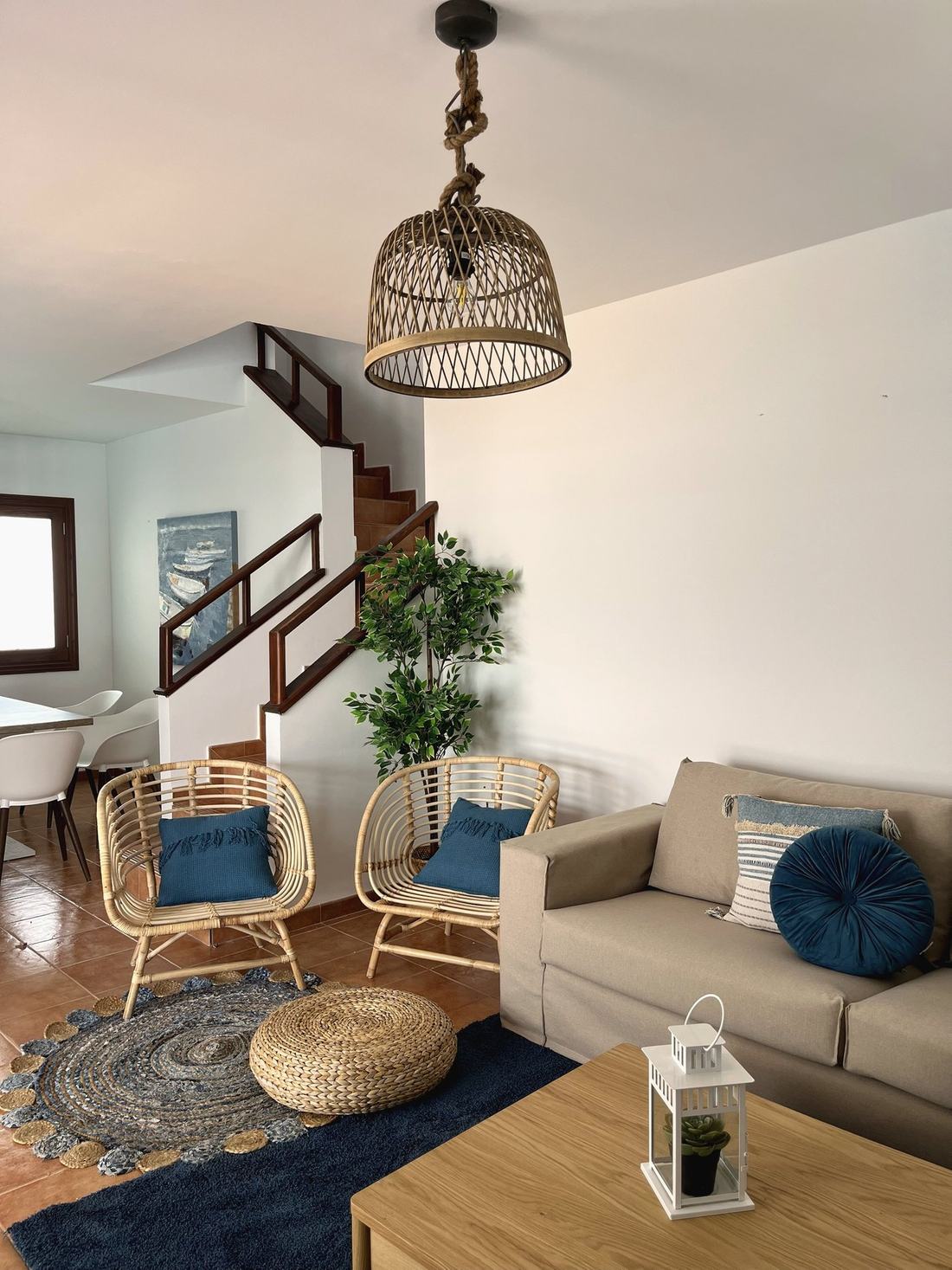 Salón con sillones de ratán, cojines azules y escalera al fondo