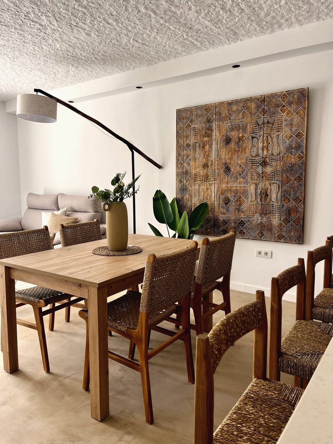 Comedor con mesa y sillas de madera y fibra, y panel tallado en la pared