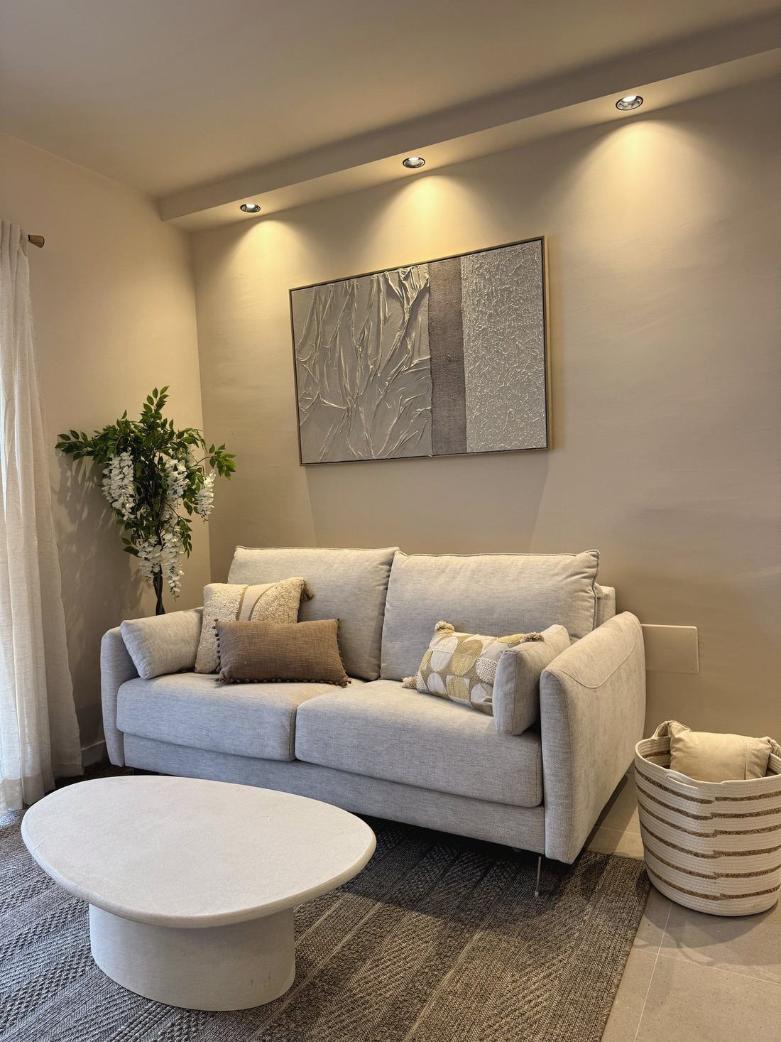 Salón con sofá gris, cuadro abstracto y planta de flores blancas