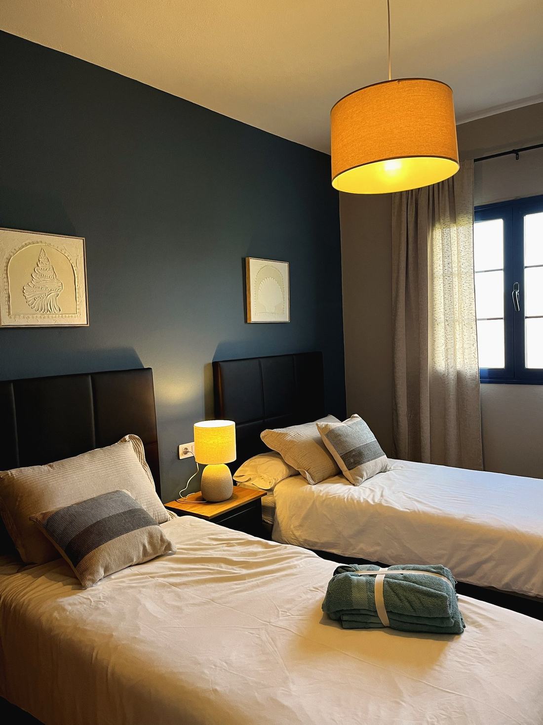 Dormitorio con dos camas, cabeceros de cuero negro y pared azul oscuro
