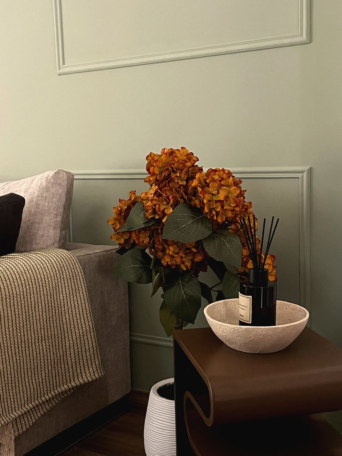 Rincón del salón con flores secas, difusor y mesa auxiliar de madera