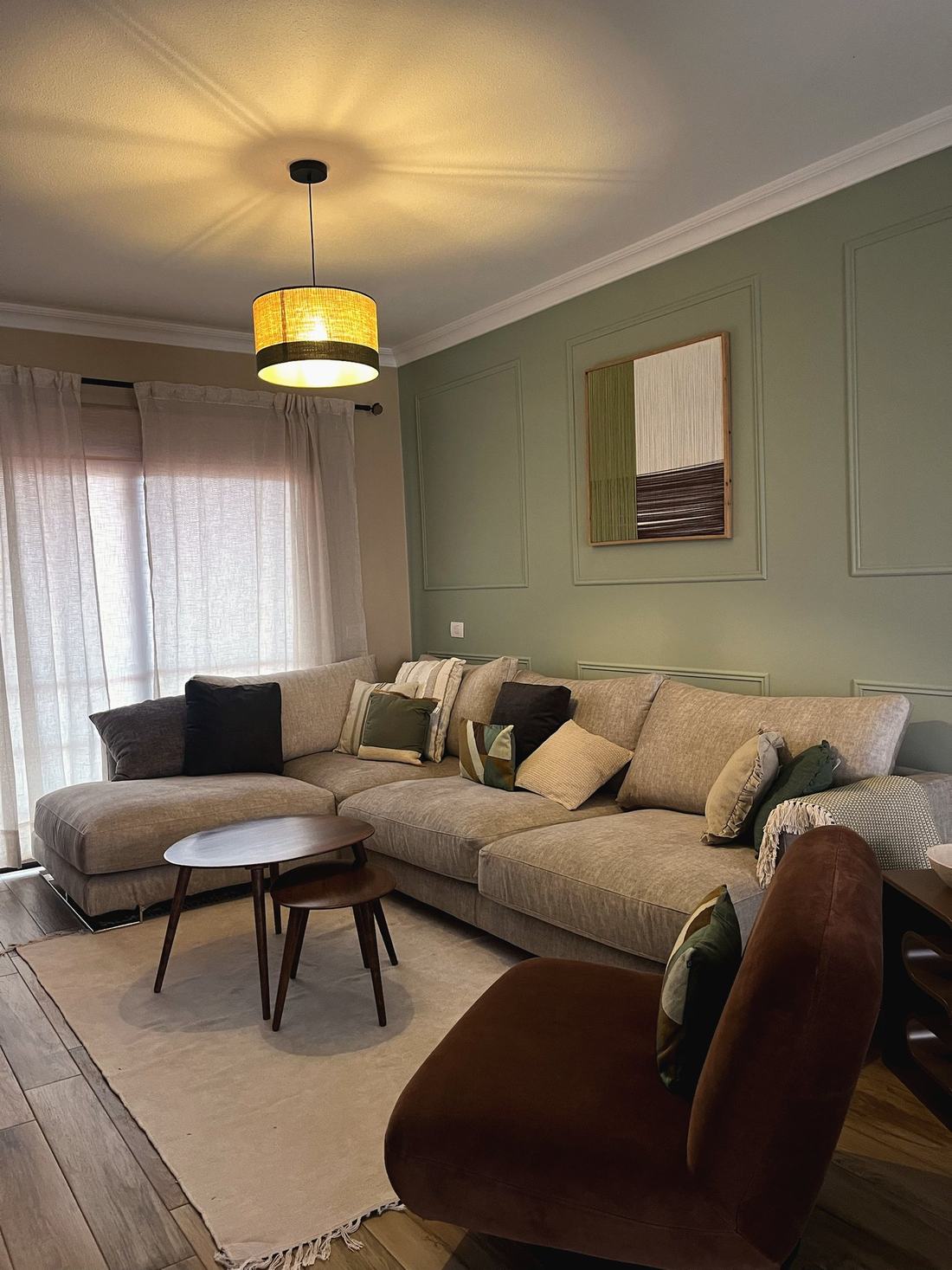 Salón en tonos verdes con sofá en L, sillón terracota y cuadro tejido